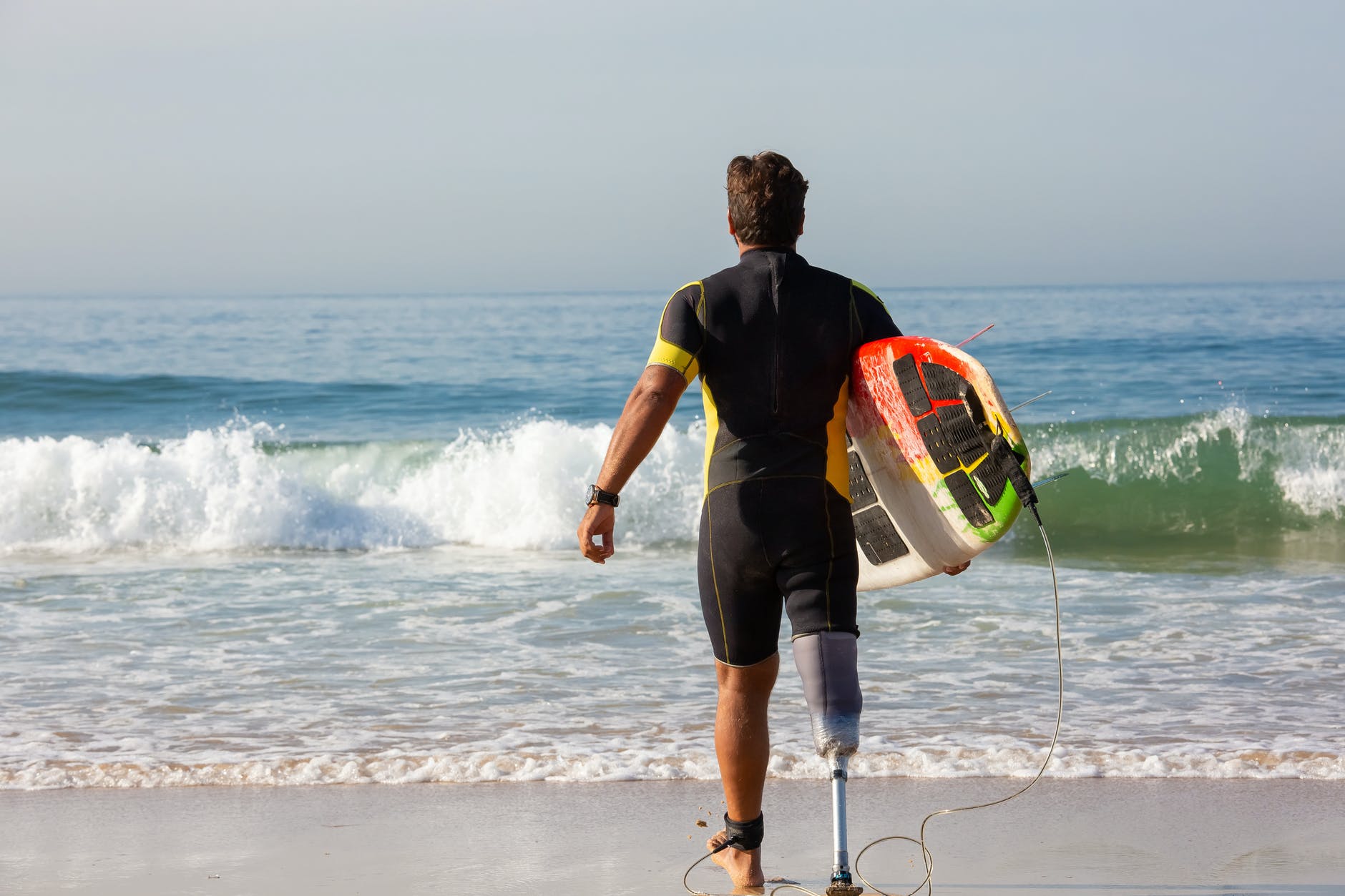 unrecognizable male surfer amputee with surfboard walking towards sea