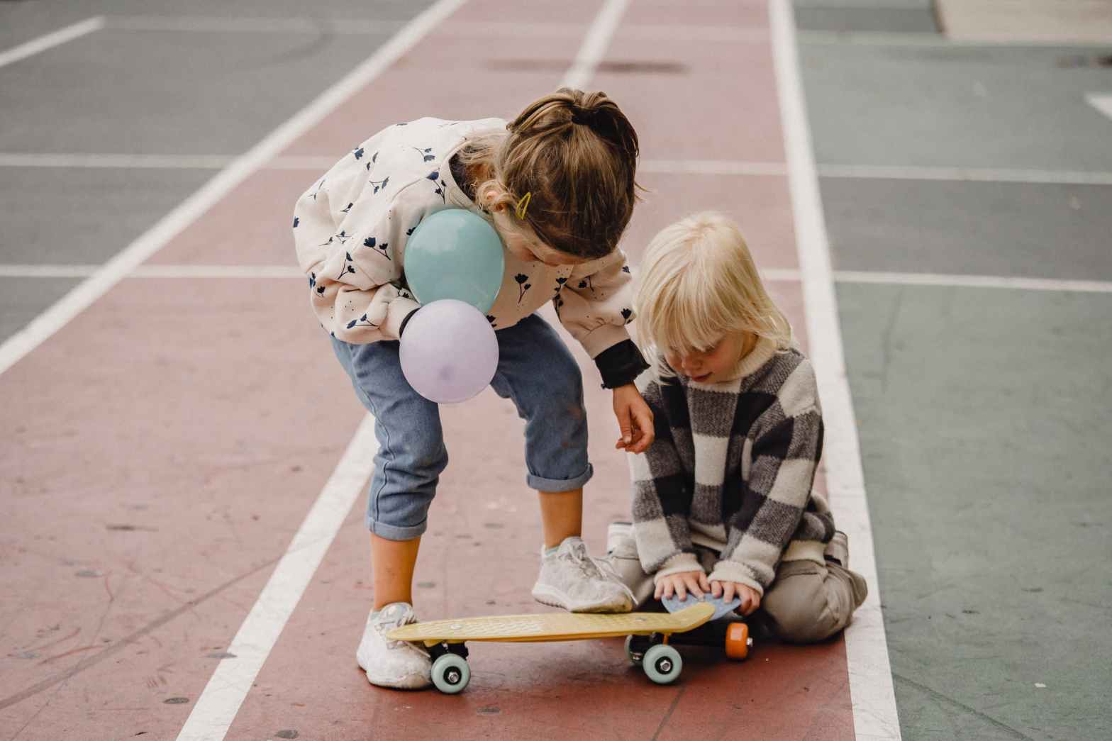 anonymous girlfriends playing with balloons and skateboard on sports ground