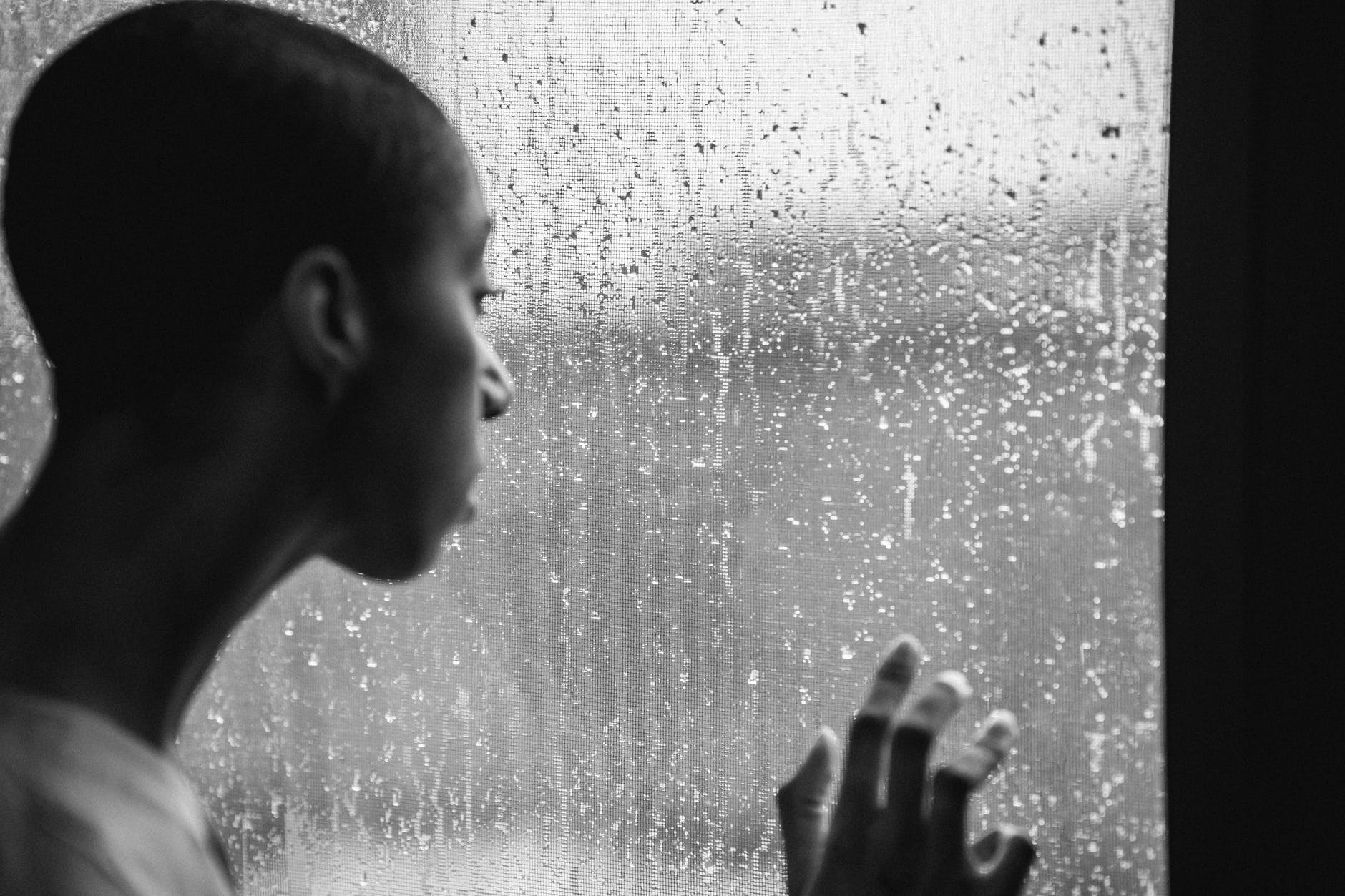 thoughtful androgynous black woman standing near window at rainy day