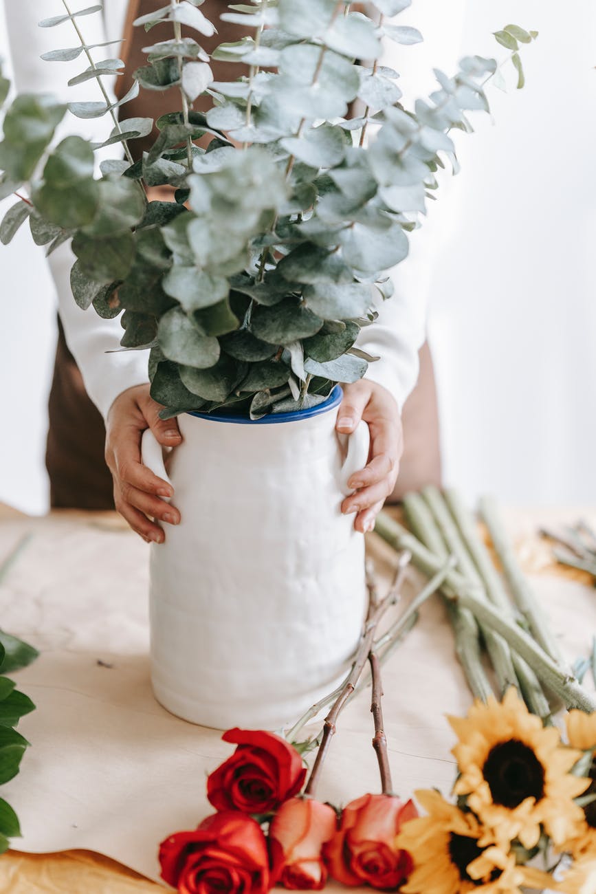 unrecognizable florist with flowers in vase and on table