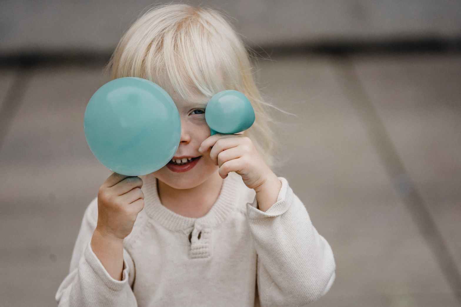 smiling little girl covering face with balloons on street